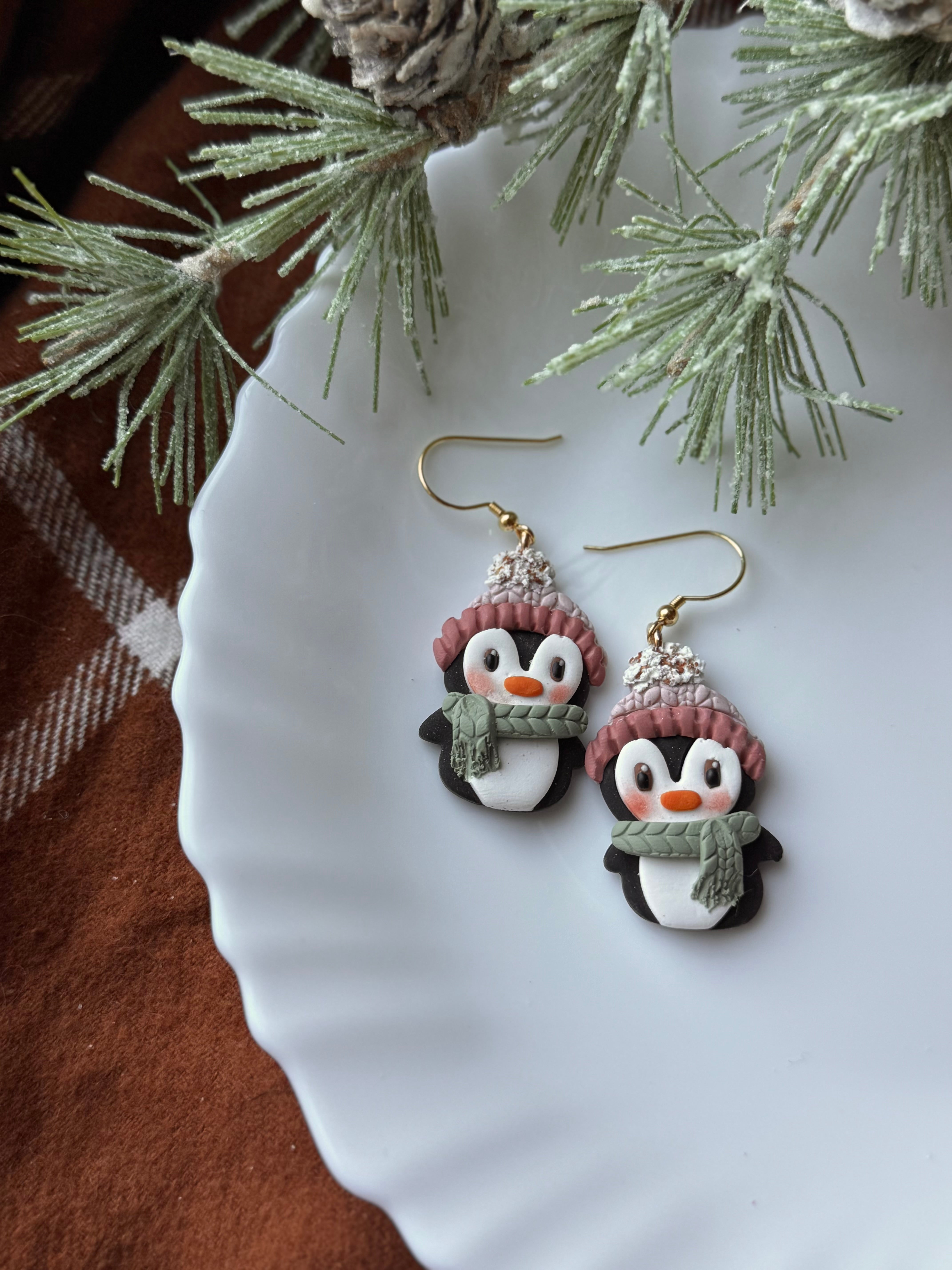 Penguin earrings on a white plate with a Christmas tree branch in the background