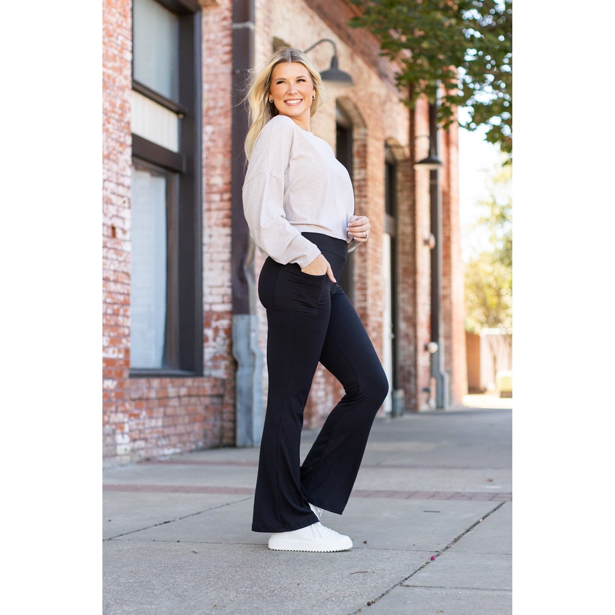Woman in a white blouse and black pants standing on a sidewalk with a brick building in the background.