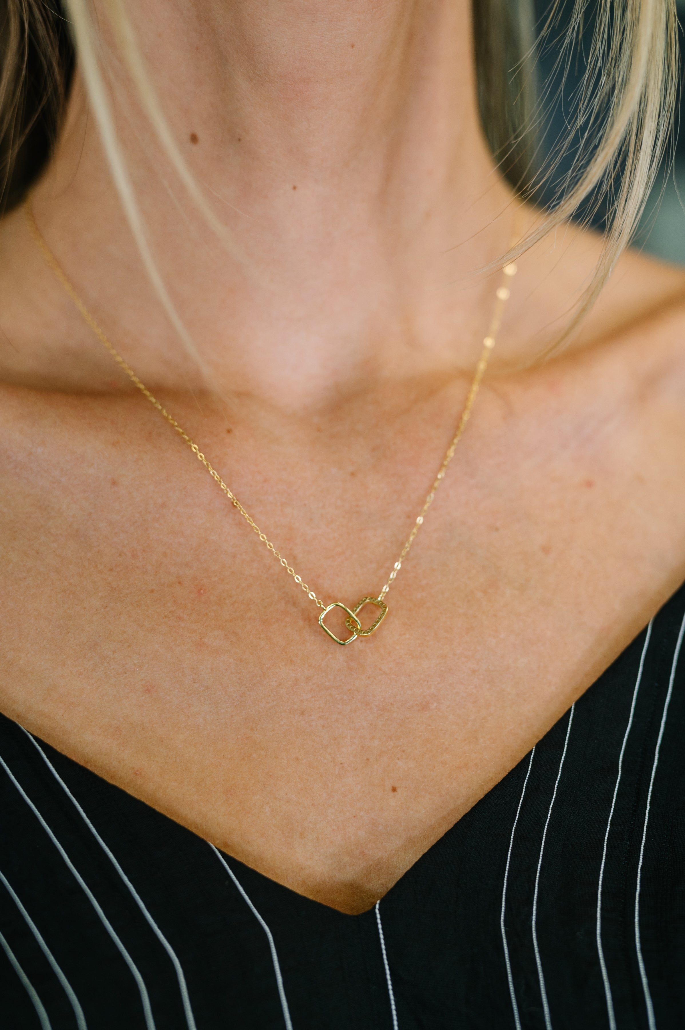 Gold necklace with a heart-shaped pendant on a person wearing a black and white striped shirt.