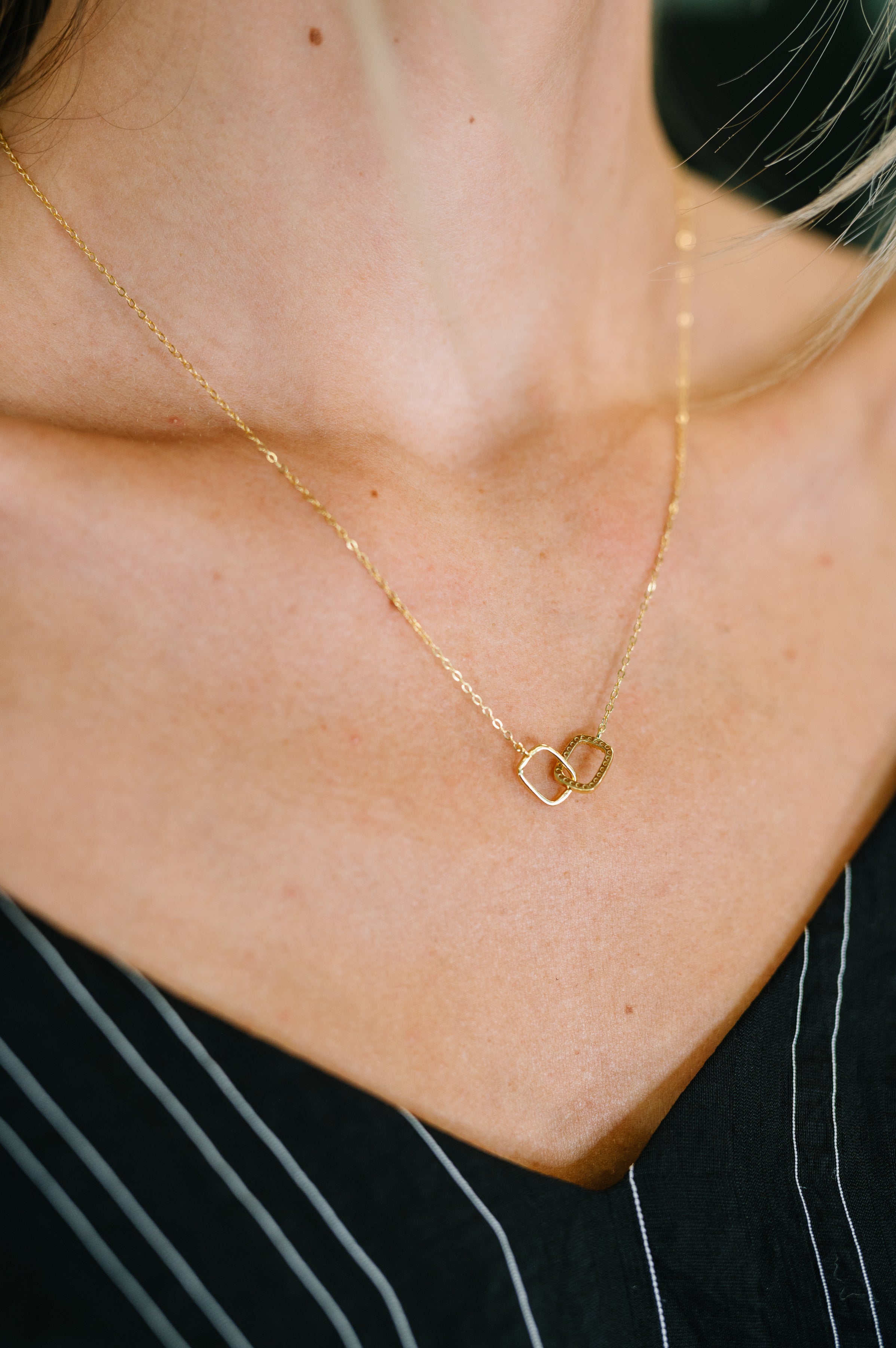 Gold necklace with a heart-shaped pendant on a person wearing a black top.