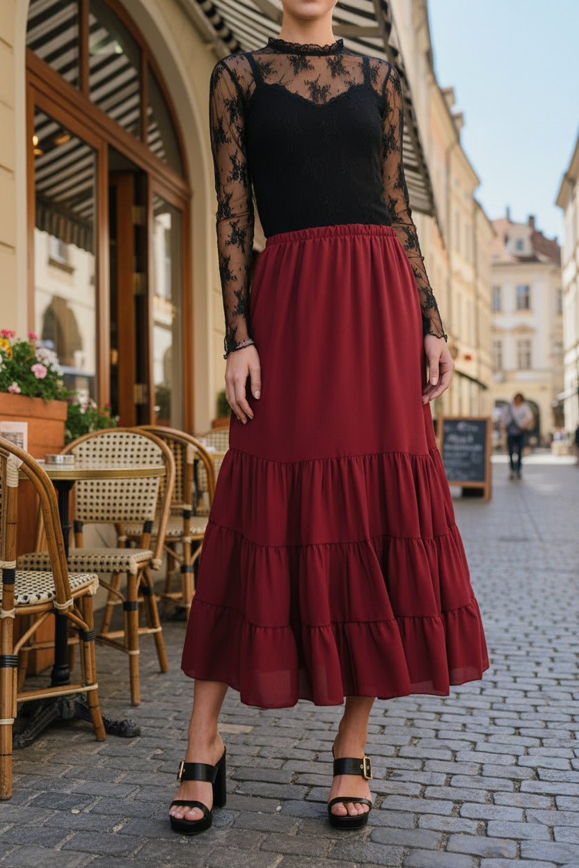 Person wearing a red tiered skirt with a black top and sandals, standing indoors.