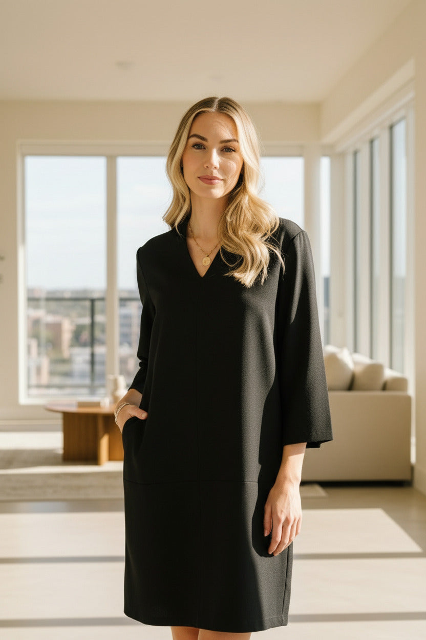 Woman in a black dress standing next to a plant indoors