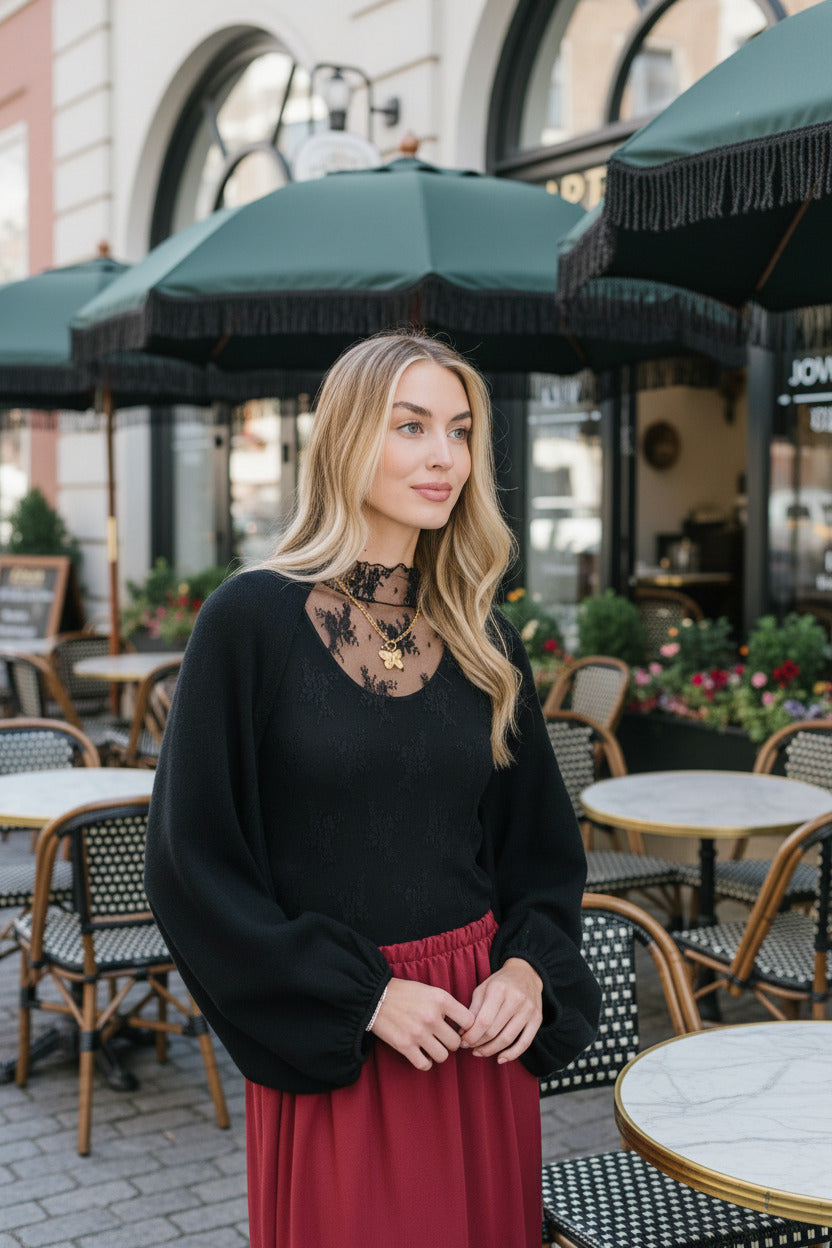 Woman wearing a black top with lace details and a red skirt indoors.