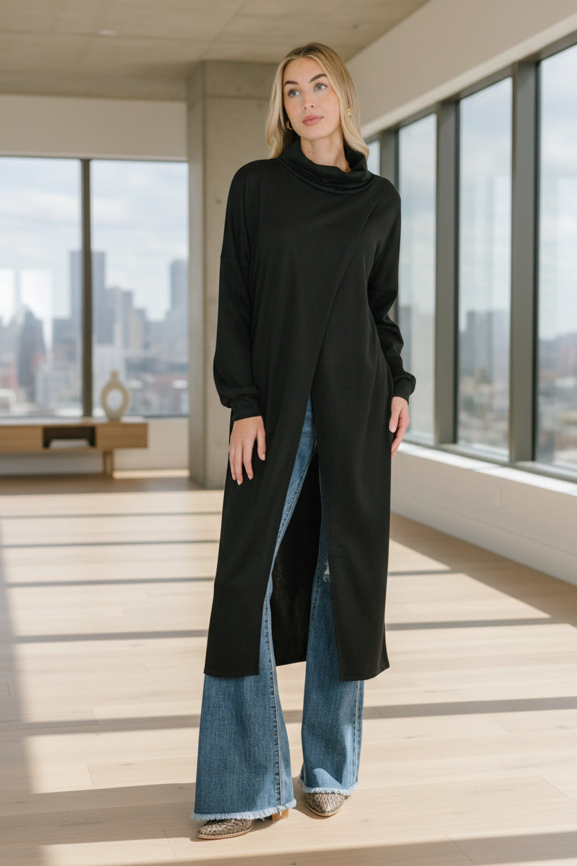 Woman wearing a long black coat over blue jeans standing indoors with decorative elements.