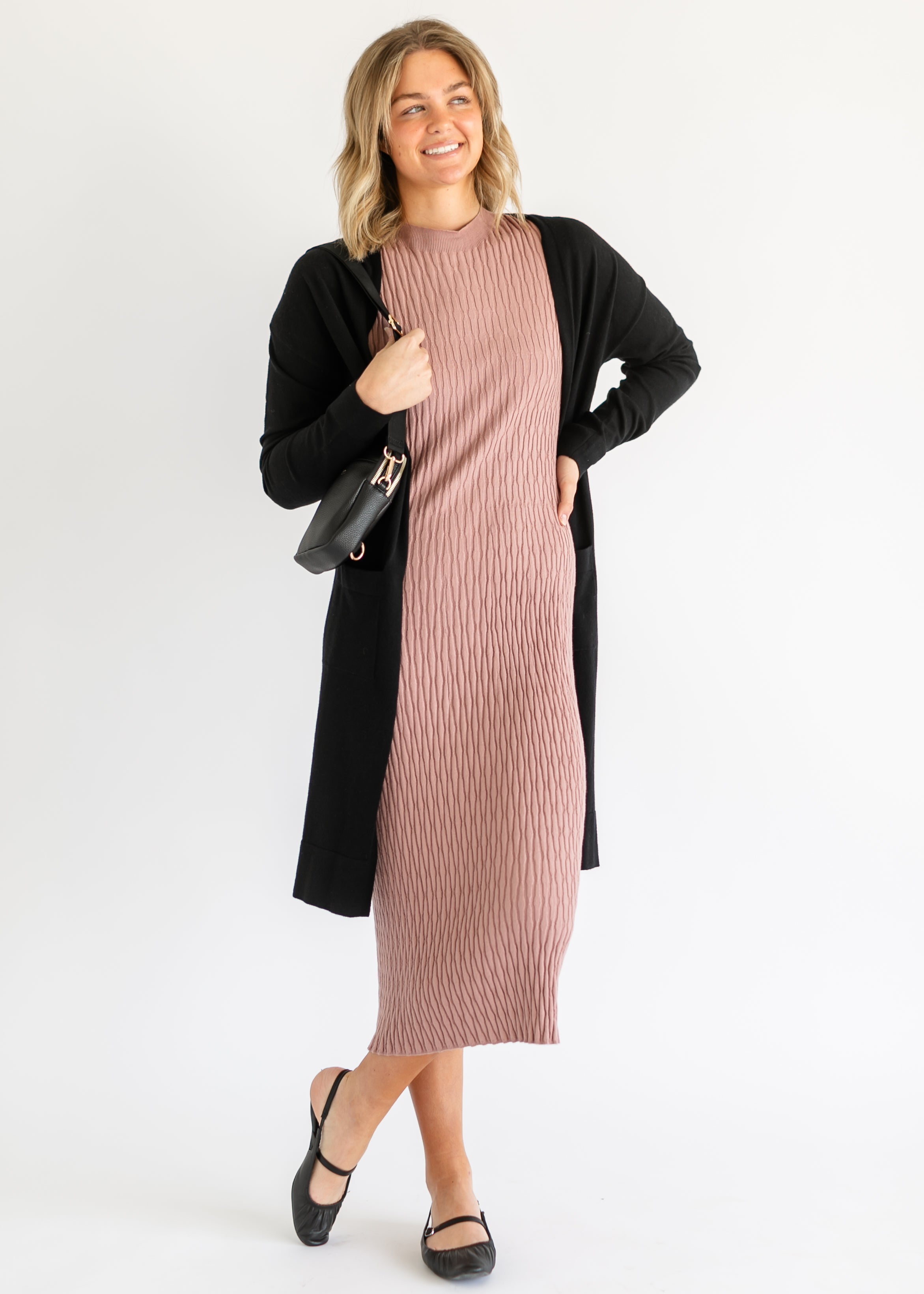 Woman wearing a pink dress with a black cardigan on a white background